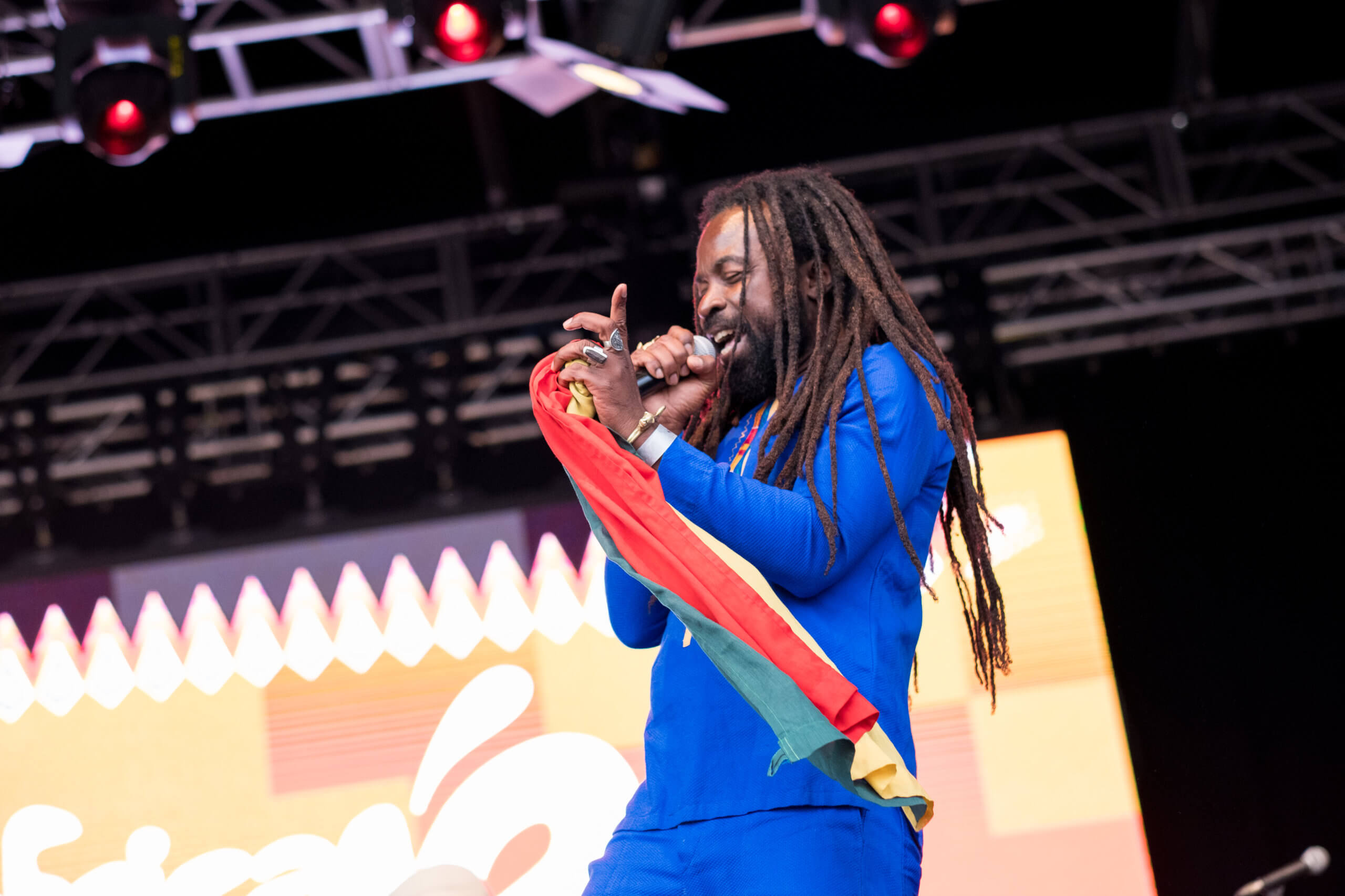 Rocky Dawuni on stage at the Africa Oyé festival in 2018. He is wearing blue clothing and is singing into a microphone.