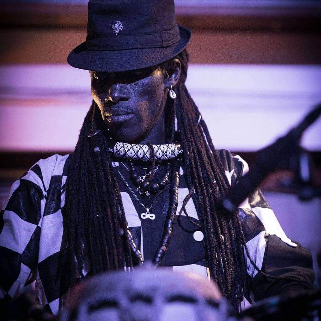 Batch Gueye - a West African Griot and singer songwriter. Playing the drums on stage in a black hat with black and white checked clothing