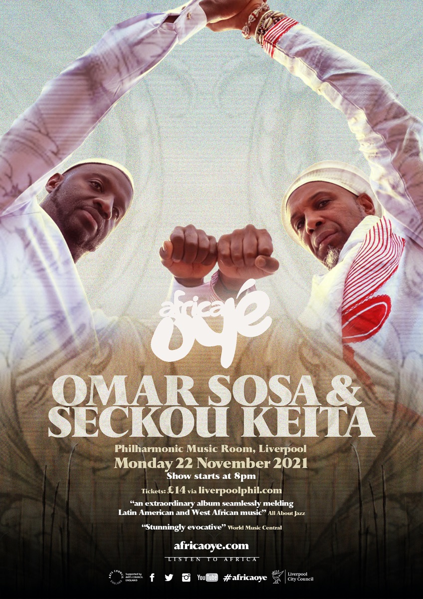 Promo image for an upcoming show. Omar Sosa and Seckou Keita stand with their fists touching, looking down at the camera. They are both wearing white.
