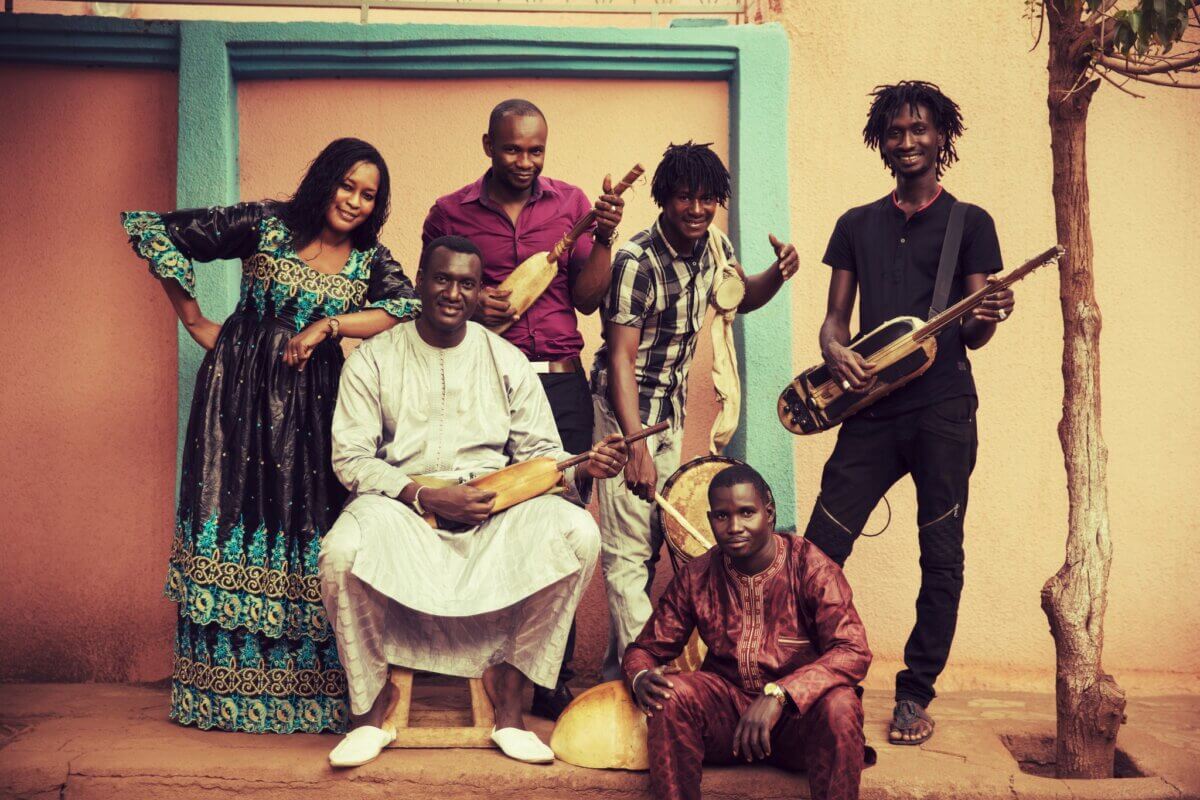 Six people posing for the camera in an outdoor setting. Some are holding musical instruments.