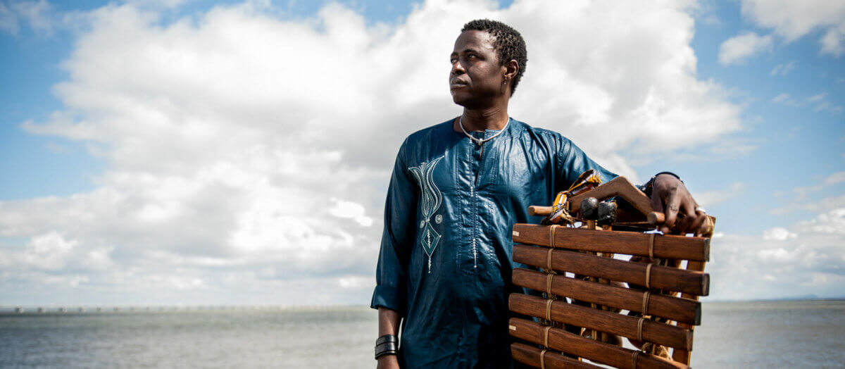 A person standing in front of the ocean holding a balafon.