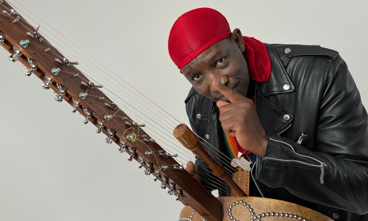 N'faly Kouyate holding a kora and putting a finger to his lips.